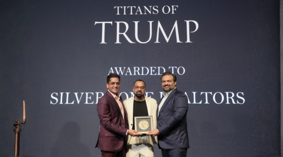 Silverstone Realtors are being honored with the “Titans of Trump” award. The event appears to celebrate excellence and outstanding performance in real estate associated with Trump-branded projects. The award is being presented on stage, with three well-dressed individuals holding the plaque and smiling for the photograph against a professional event backdrop.